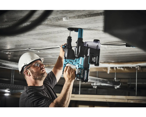 Un homme perce un plafond en béton avec un perforateur à batterie Makita.