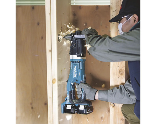 Ein Mann bohrt mit einer blauen Akku-Kernbohrmaschine ein Loch in ein Holzbrett.