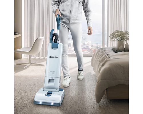 Une personne utilise un aspirateur Makita dans une chambre. L''aspirateur est équipé d''un filtre HEPA.