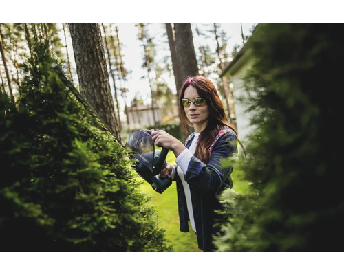 Une femme coupe une haie avec un taille-haie dans le jardin.