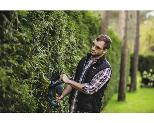 Un homme taille une haie dans le jardin avec un taille-haie à batterie.