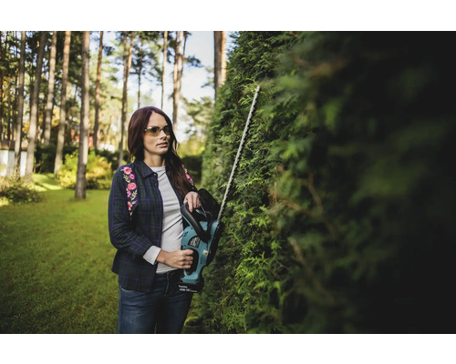Une femme taille une haie avec un taille-haie dans le jardin.
