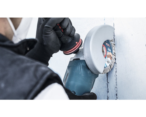 Eine Person benutzt einen Winkelschleifer an einer Wand.