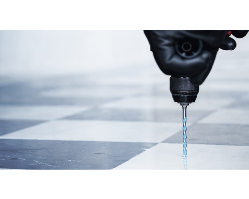 Eine Bohrmaschine mit einem Steinbohrer bohrt ein Loch in eine Fliese.