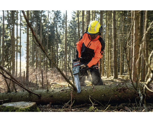 Une personne portant des vêtements de protection coupe un tronc d''arbre avec une tronçonneuse dans une forêt.