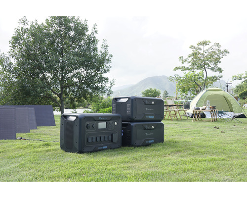 Szene mit tragbaren Bluetti-Kraftwerken, Solarmodulen und einem Zelt auf einer Wiese.
