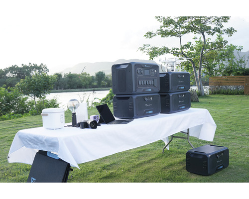 Aufnahme einer Szene im Freien mit mehreren tragbaren Bluetti-Kraftwerken auf einem Tisch, zusammen mit verschiedenen Geräten