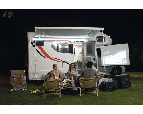 Eine Familie genießt einen Filmabend im Freien mit einem Wohnmobil, einem Projektor und einer Leinwand.