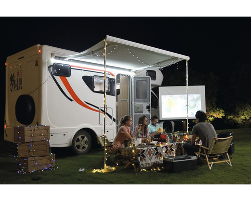Szene im Freien mit Wohnmobil, Markise, Lichterketten und Personen beim Betrachten einer Leinwand