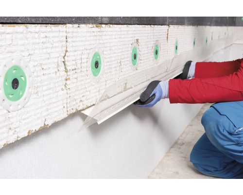 Une personne installe un profilé de socle sur une façade avec isolation thermique
