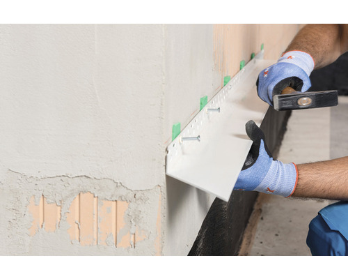 Handwerker befestigt Sockelschutzprofil mit Hammer und Schrauben an der Wand.