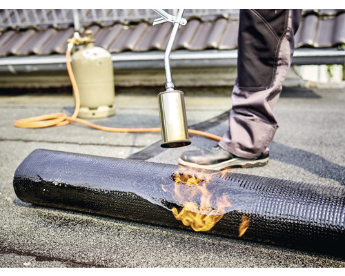 Dachdecker verschweißt Bitumenbahn mit einem Schweißbrenner, Gasflasche im Hintergrund
