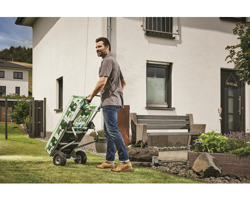 Un homme transporte des caisses de boissons avec un diable dans le jardin.