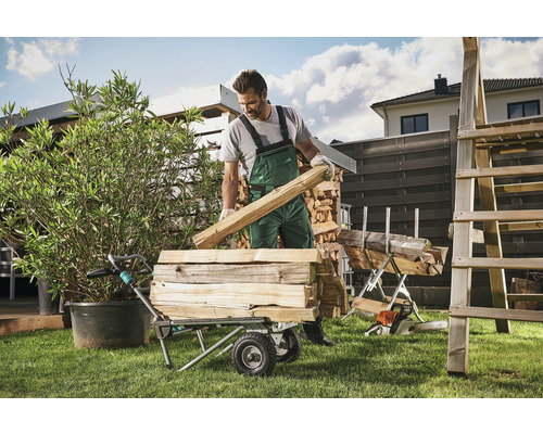 Un homme charge une brouette de bois de chauffage dans le jardin.