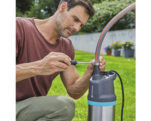 Mann befestigt einen Gartenschlauch mit einem Schraubenzieher an einer Gardena Pumpe.