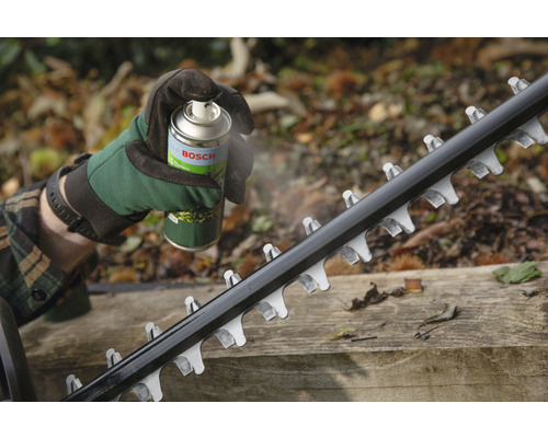 Une personne vaporise un spray d''entretien Bosch sur la lame d''un taille-haie.