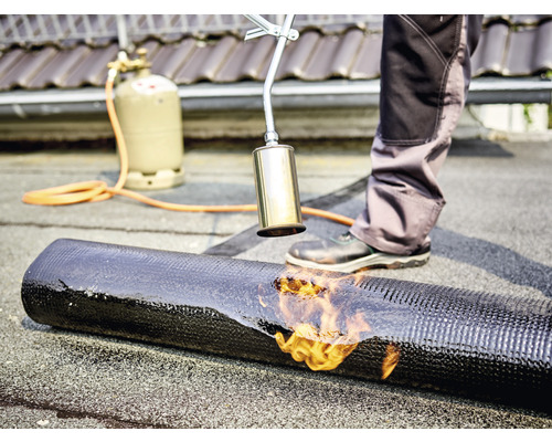 Dachdecker schweisst mit einem Gasbrenner eine Dachbahn auf ein Dach