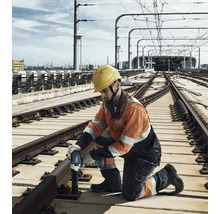 Ein Bauarbeiter mit Schutzhelm benutzt einen Akku-Schlagschrauber an Bahngleisen.