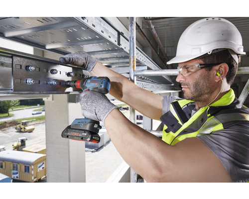 Ein Handwerker mit Schutzhelm und Schutzbrille arbeitet mit einem Akku-Bohrschrauber an einer Metallkonstruktion.