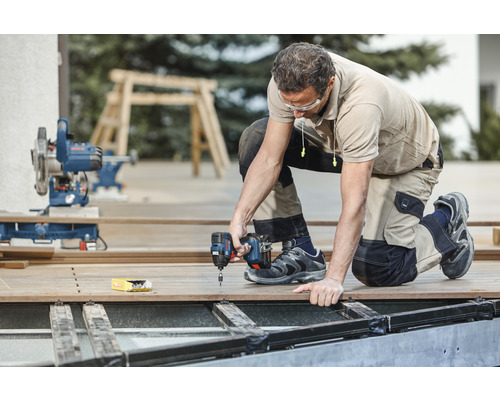 Ein Handwerker kniet auf einer Terrasse und arbeitet mit einem Akku-Schlagschrauber.