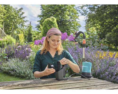 Frau reinigt eine Gardena Schmutzwasserpumpe auf einem Gartentisch im Garten.