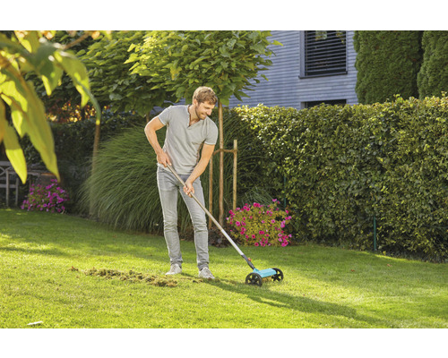 Ein Mann benutzt einen Rasenkehrer im Garten, um Rasenabfälle zu entfernen.