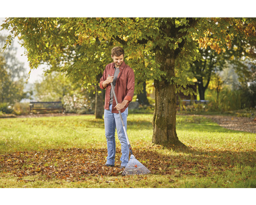 Homme ratissant les feuilles mortes dans le jardin, feuilles d''automne sur la pelouse.