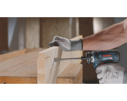 Une personne perce un trou dans une planche en bois avec une perceuse-visseuse sans fil.