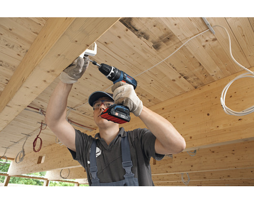 Un artisan fixe un support à un plafond en bois à l''aide d''une visseuse sans fil.
