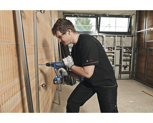 Handwerker bohrt mit einem Akku-Bohrschrauber ein Loch in eine Wand, auf der Metallprofile angebracht sind.