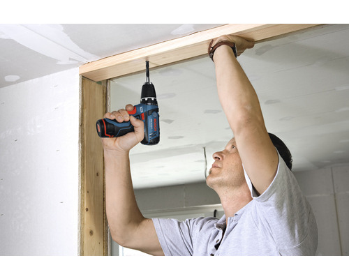 Ein Mann befestigt mit einem Akku-Bohrschrauber eine Holzleiste an der Decke.