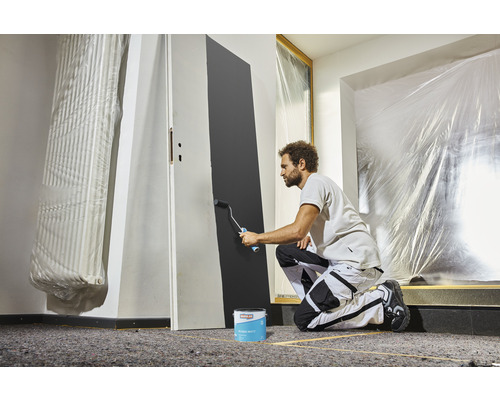 Mann streicht eine Tür mit einem Farbroller und Farbe