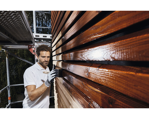 Mann streicht Holzfassade mit Holzschutzlasur.