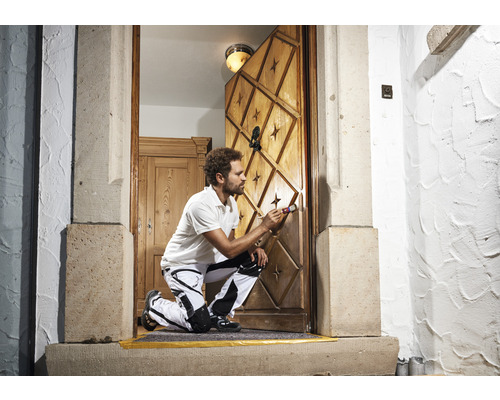 Un artisan peint une porte en bois avec des motifs d''étoiles et des ornements à l''aide d''un pinceau.