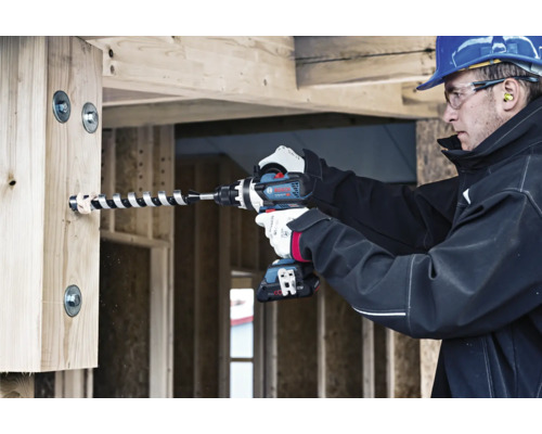 Ein Handwerker bohrt mit einem Akku-Bohrschrauber ein Loch in einen Holzbalken.