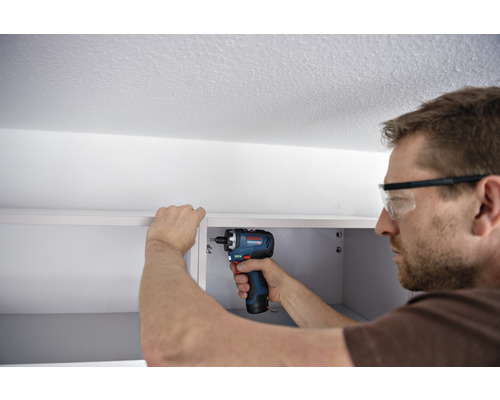 Mann montiert mit einem Akku-Bohrschrauber einen Schrank.