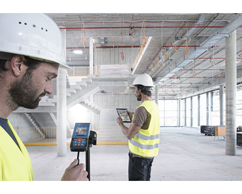 Deux ouvriers du bâtiment utilisent un télémètre laser numérique et une tablette sur un chantier de construction.