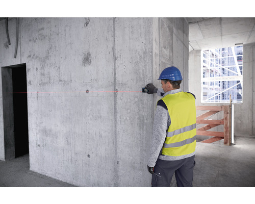 Un ouvrier du bâtiment utilise un niveau laser sur un mur en béton sur un chantier de construction.
