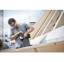 Mann schraubt mit einem Akku-Bohrschrauber Holzlatten auf einem Dachstuhl fest