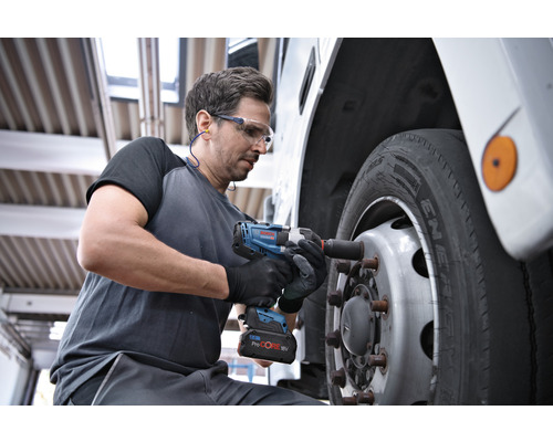 Un homme utilise une clé à choc sans fil pour fixer une roue sur un véhicule.