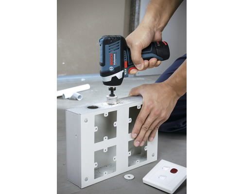 Une personne perce un trou dans un boîtier métallique avec une perceuse-visseuse sans fil.