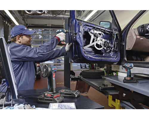 Werkstatt-Szene mit einem Handwerker, der mit einem Akku-Bohrschrauber an einer Autotür arbeitet, im Vordergrund Akku-Winkelschleifer und Akku-Schlagschrauber.