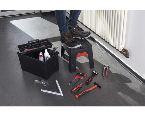 Werkzeugkiste, Tritthocker und verschiedene Werkzeuge auf dem Boden, Person mit Sicherheitsschuhen steht auf dem Tritthocker.