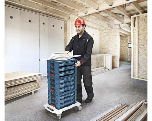 Un artisan pousse un chariot à outils à plusieurs tiroirs dans un bâtiment en construction.