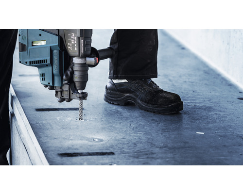 Ein Mann bohrt mit einem Bohrhammer ein Loch in eine Betonplatte.