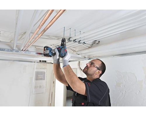 Handwerker bohrt mit einem Akku-Bohrschrauber Löcher in eine Decke für die Installation von Rohren und Leitungen.