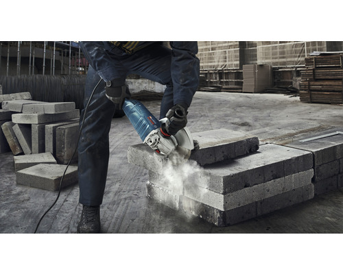 Un homme coupe un bloc de béton avec une meuleuse d''angle.