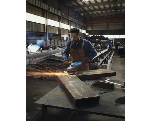 Un homme portant des lunettes de protection et des gants meule du métal avec une meuleuse d''angle dans un atelier.