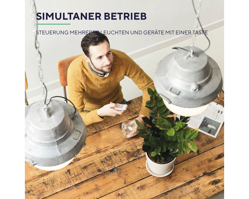 Mann steuert mehrere Leuchten mit einer Fernbedienung an einem Holztisch.