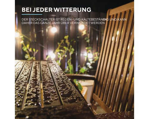 Ein Holztisch und ein Stuhl stehen draußen im Regen, eine Lichterkette hängt im Hintergrund
